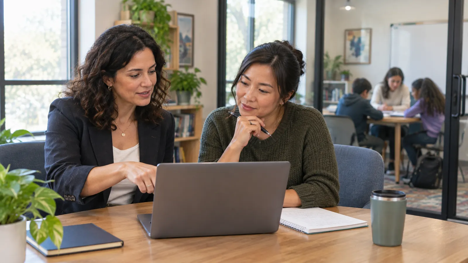 Two tutoring directors discussing options at a laptop with a second tutoring room visible behind them